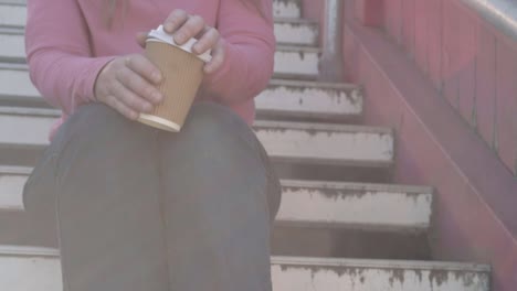 Woman-sitting-on-steps-drinking-take-out-coffee-medium-shot