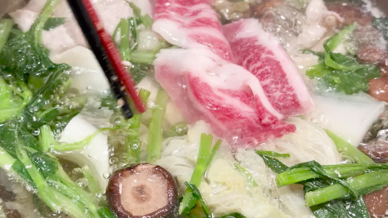 Marbled wagyu beef slices cooked in boiling broth with mushrooms, greens, and chopsticks, overhead view