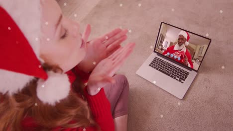 Animation-Von-Schnee,-Der-über-Eine-Glückliche-Kaukasische-Frau-Mit-Weihnachtsmütze-Auf-Einem-Laptop-Videoanruf-Mit-Der-Familie-Fällt