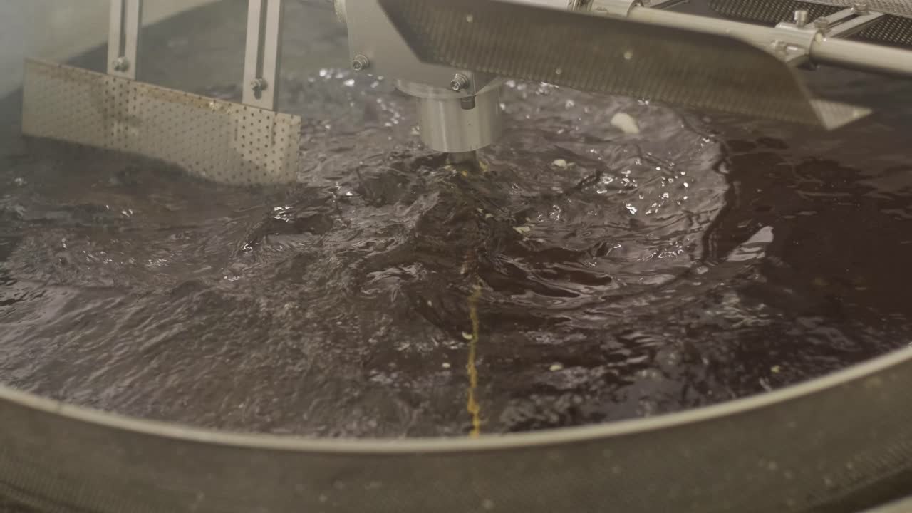 производство картофельных чипсов и закусок. промышленная машина для глубокой обжаривания. чипсы обжариваются в большой миске с маслом. производственная заводская линия перемещает золотые картофельные чипсы после обжарития.