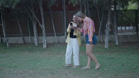 two women looking at a smartphone in a park