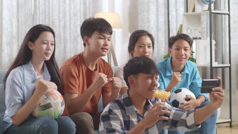 asian teenagers cheering and watching football game on smart phone and celebrating victory at home