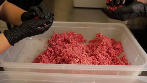 couple of chefs with black latex gloves preparing minced meat for burgers, close up shot