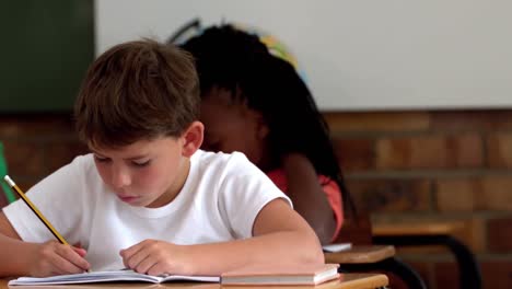 Little-boy-writing-in-notepad-in-classroom