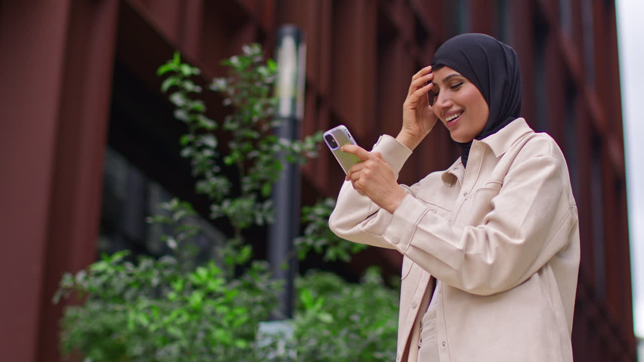 Muslim Businesswoman Wearing Hijab Standing Outside Modern Office Getting Good News About Job Offer Or Promotion On Mobile Phone