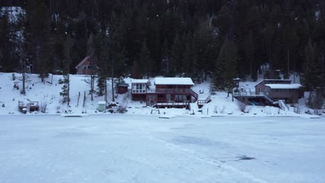 This-beautiful-wooden-Lakehouse-covered-in-snow-sits-next-to-a-frozen-lake-and-a-dense-forest-in-British-Columbia