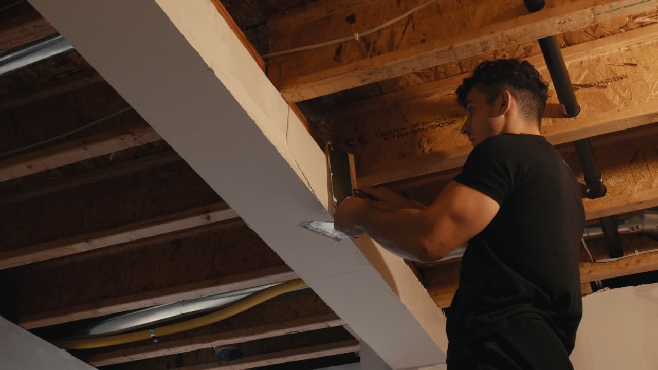 Un giovane intonaca con cura una trave sul soffitto