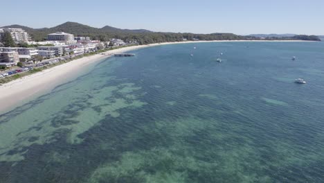 flying over the clear water of shoal bay with sailing boats in summer in nsw, australia