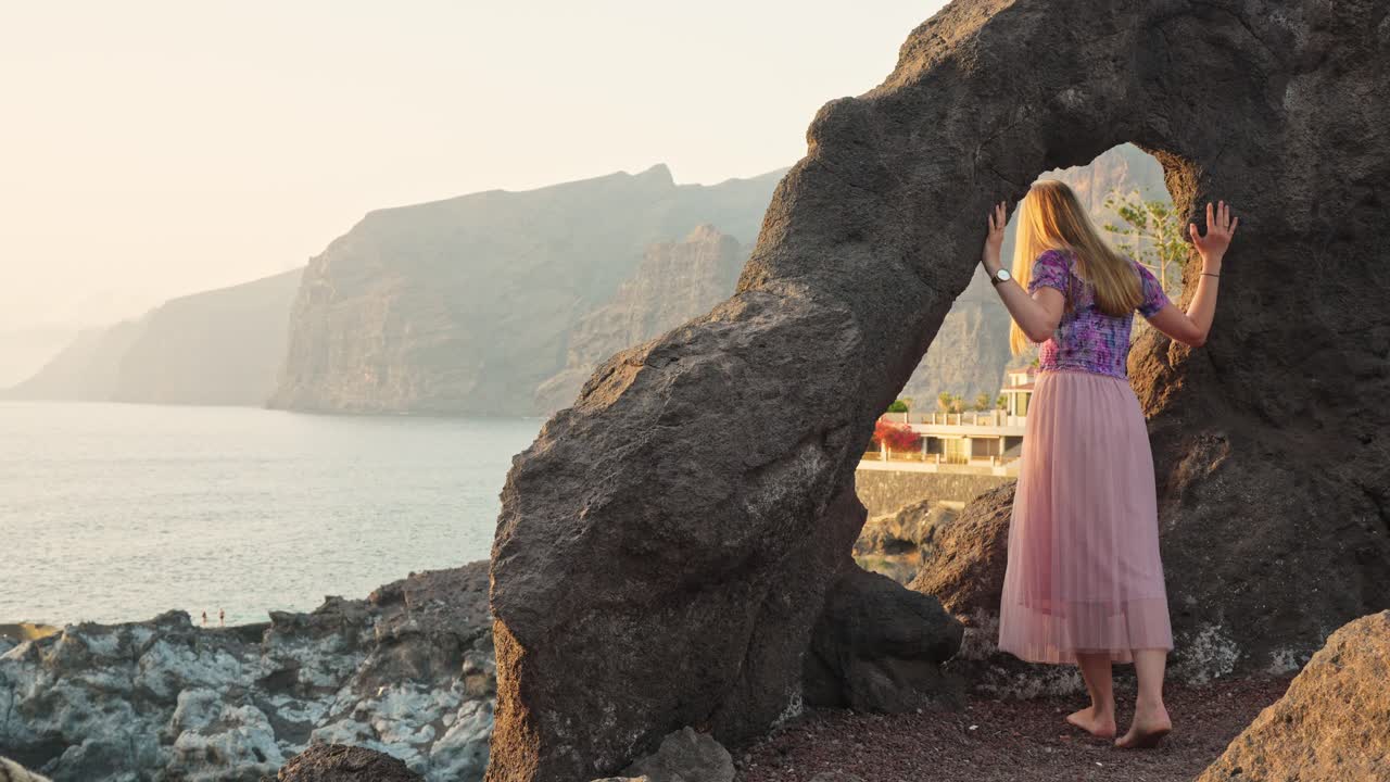 Tourist woman leans inside natural rock arch formation, Tenerife, golden hour