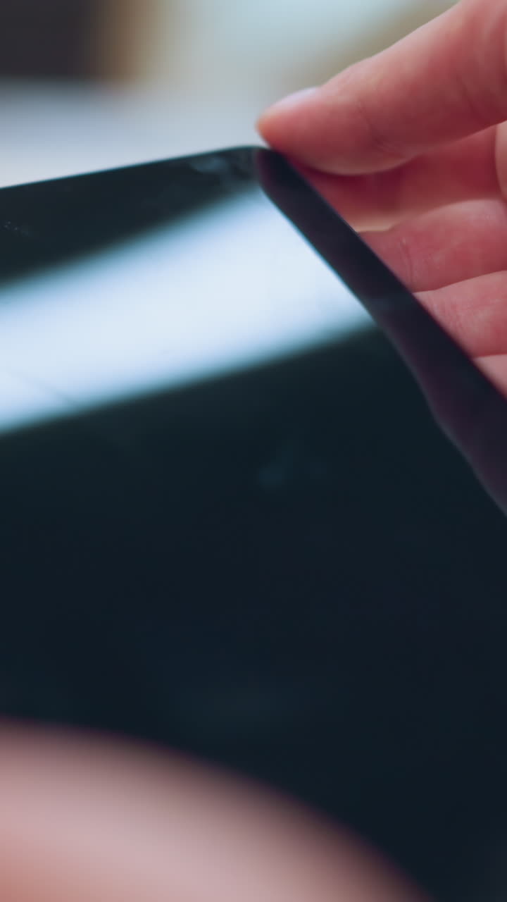 전자제품 가게에서 태블릿을 들고 있는 여성은 보안 케이블로 연결되어 있으며, 화면에서 빛이 반사되는 동안 천천히 장치를 검사합니다.