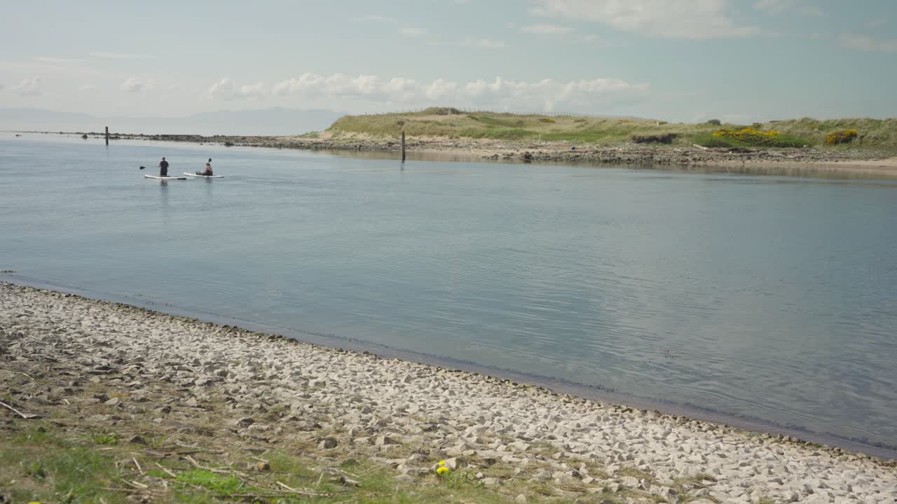Two people near the coastline rowing canoes out to sea, wide shot