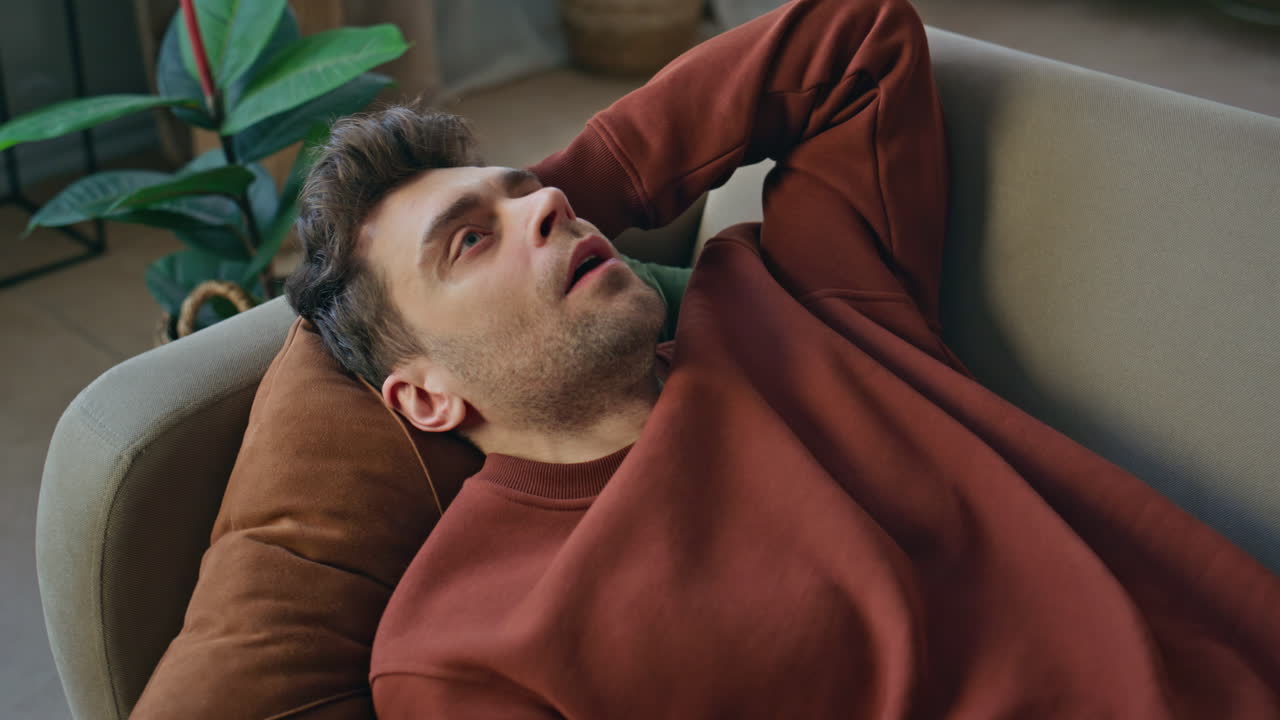 Tired man falling couch feeling exhausted close up. Guy looking on smartphone