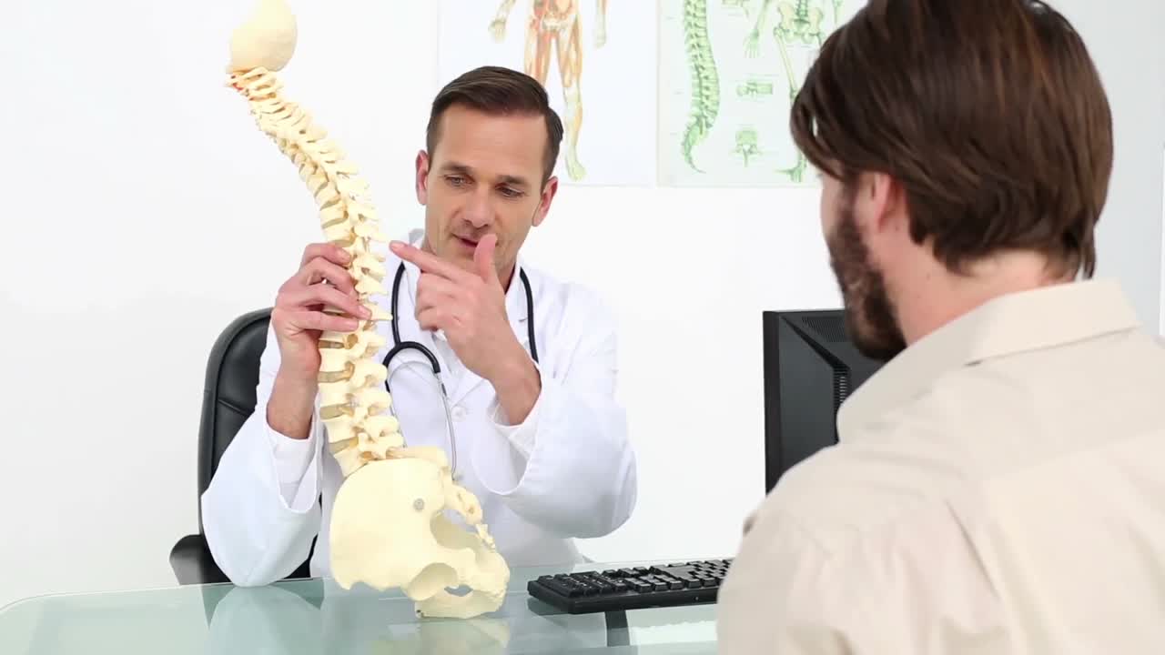 médico mostrando a su paciente un modelo de una columna vertebral