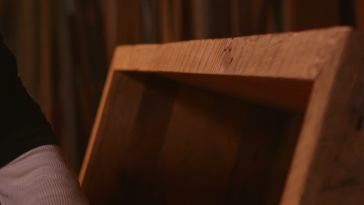 Un falegname leviga i ripiani di una libreria di legno.