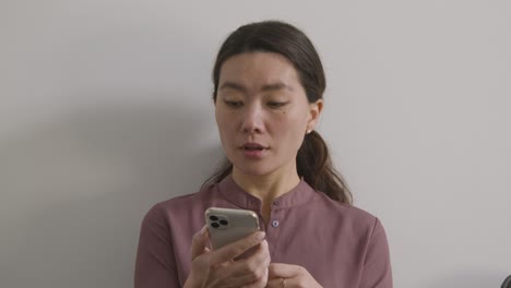 Nervous Female Candidate Wearing Suit In Office Waiting For Job Interview Looking At Mobile Phone 