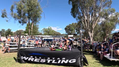 wrestlers competing in an outdoor ring, audience watching.