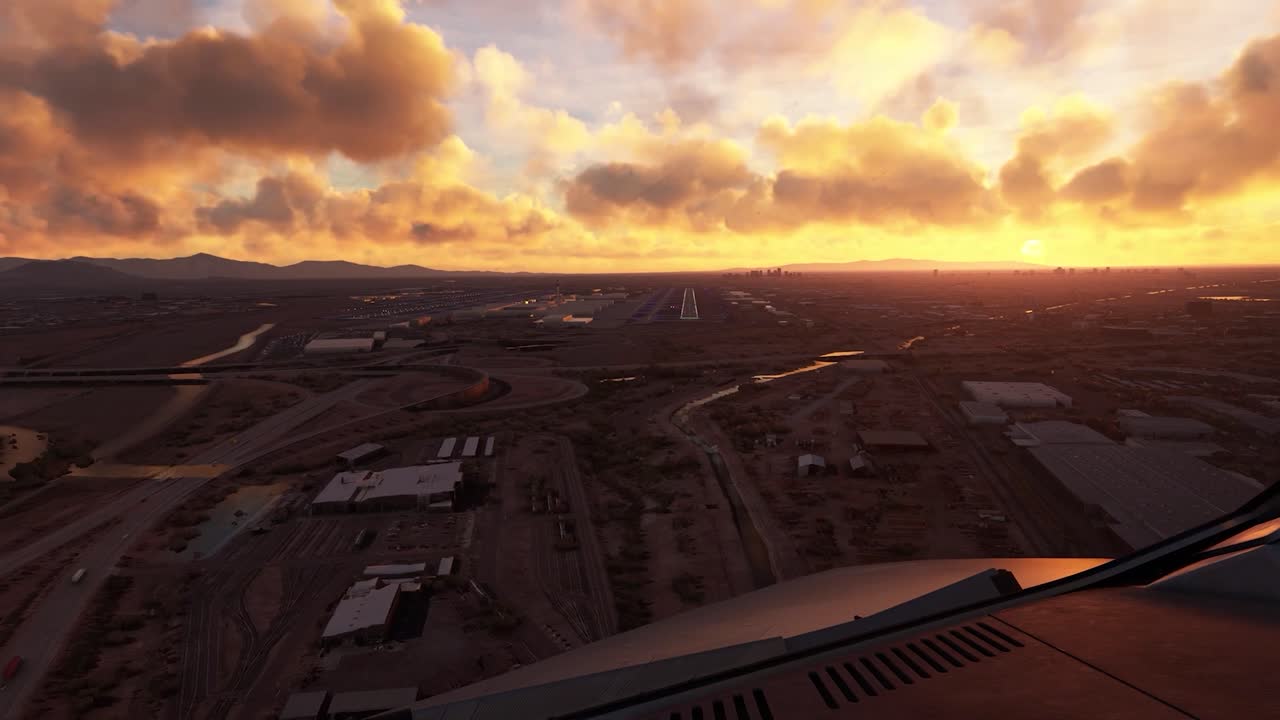 FPV or first person view from inside a small airplane flying over a small city with roads and houses, approaching slowly to a landing strip at an airport and begins to land. Orange sunset or sunrise.