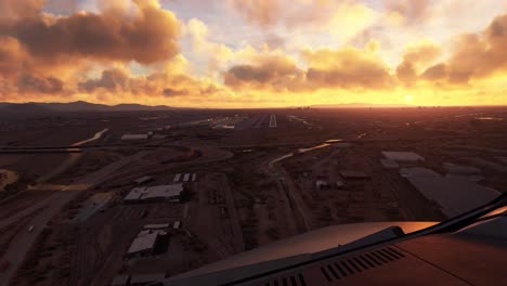 fpv or first person view from inside a small airplane flying over a small city with roads and houses, approaching slowly to a landing strip at an airport and begins to land. orange sunset or sunrise.