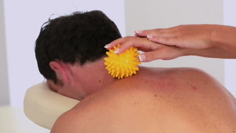 masajista usando una bola de masaje amarilla en el cuello del cliente