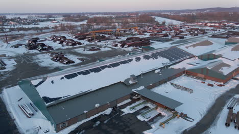 Flying-towards-industrial-warehouse-with-snow-covered-solar-panels-on-rooftop