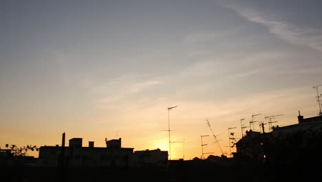 panning movement of the camera on the balcony, view of rooftops buildings in silhouette and sunset orange and cloudy blue sky on the background