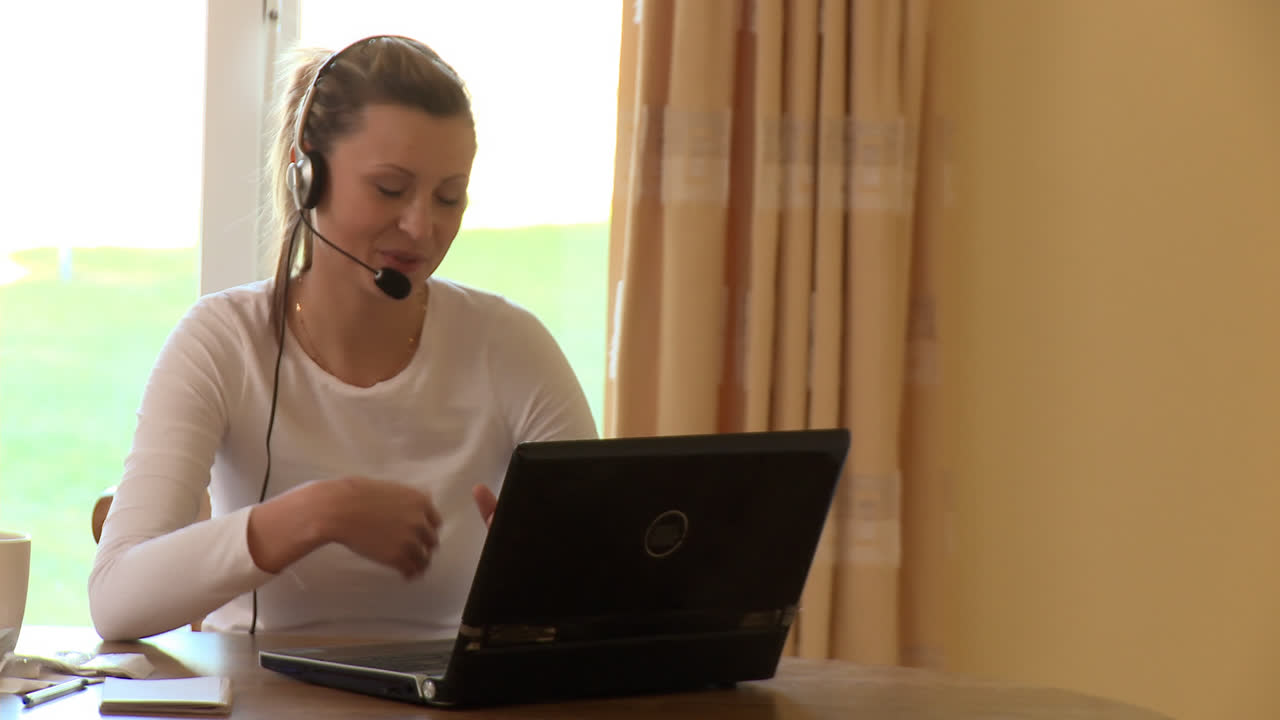 Glad kvinde med headset på bruger en bærbar computer