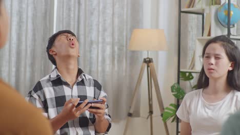 close up of asian teen group sitting in chairs forming a circle playing game on smartphone at home. disappointed loosing game with upset face