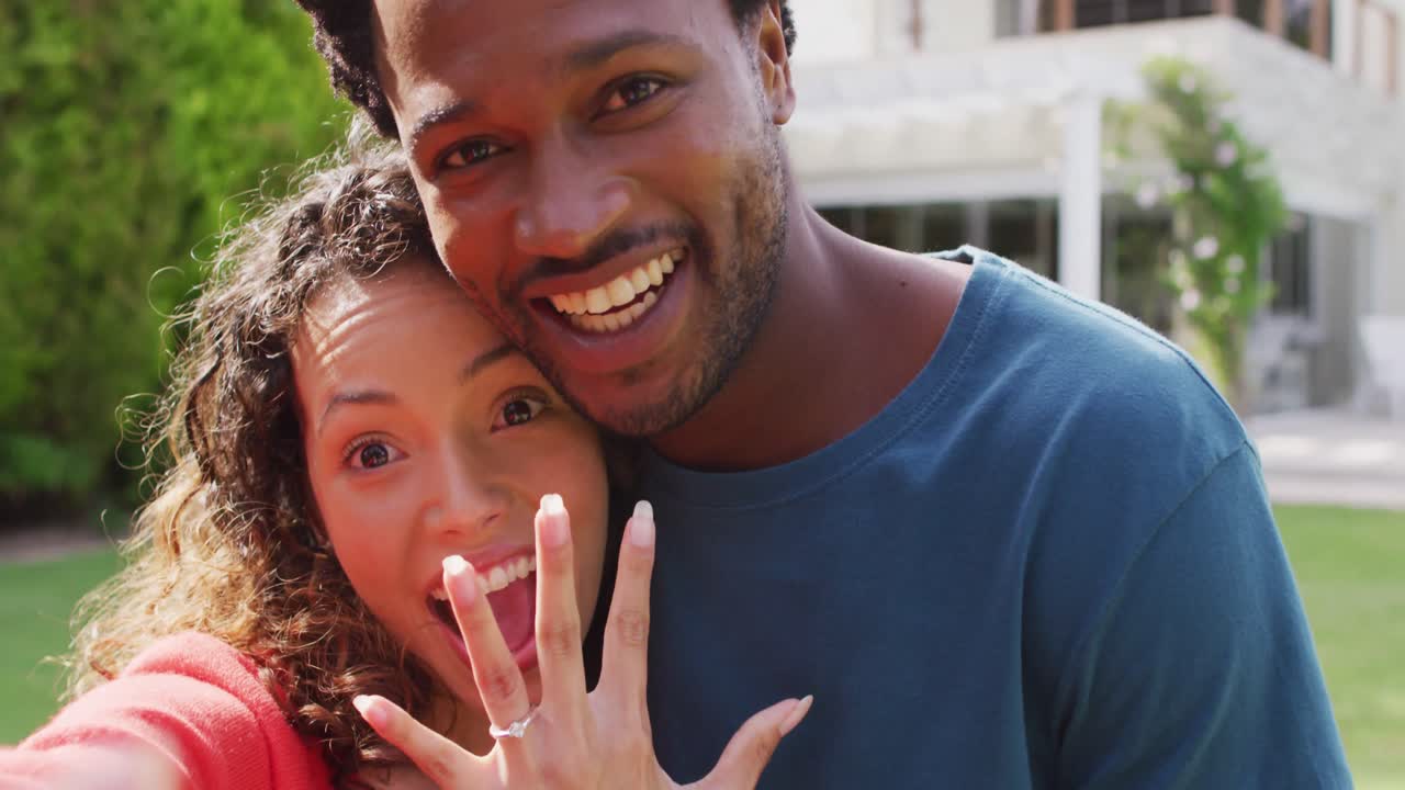 Happy biracial couple taking selfie in garden after proposal