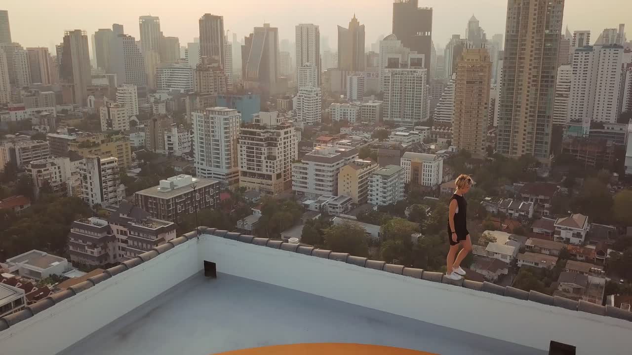 Drone view from helipad rooftop in Bangkok showing sunset skyline warm light over dense high rise buildings wide city panorama and elevated urban perspective with lone person