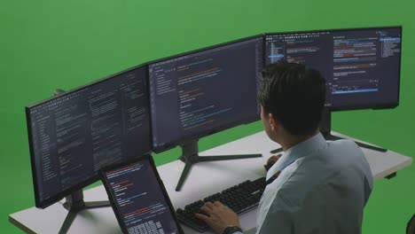 vista lateral de un desarrollador asiático trabajando con una tableta mientras escribe código con múltiples pantallas de computadora en el estudio de pantalla verde