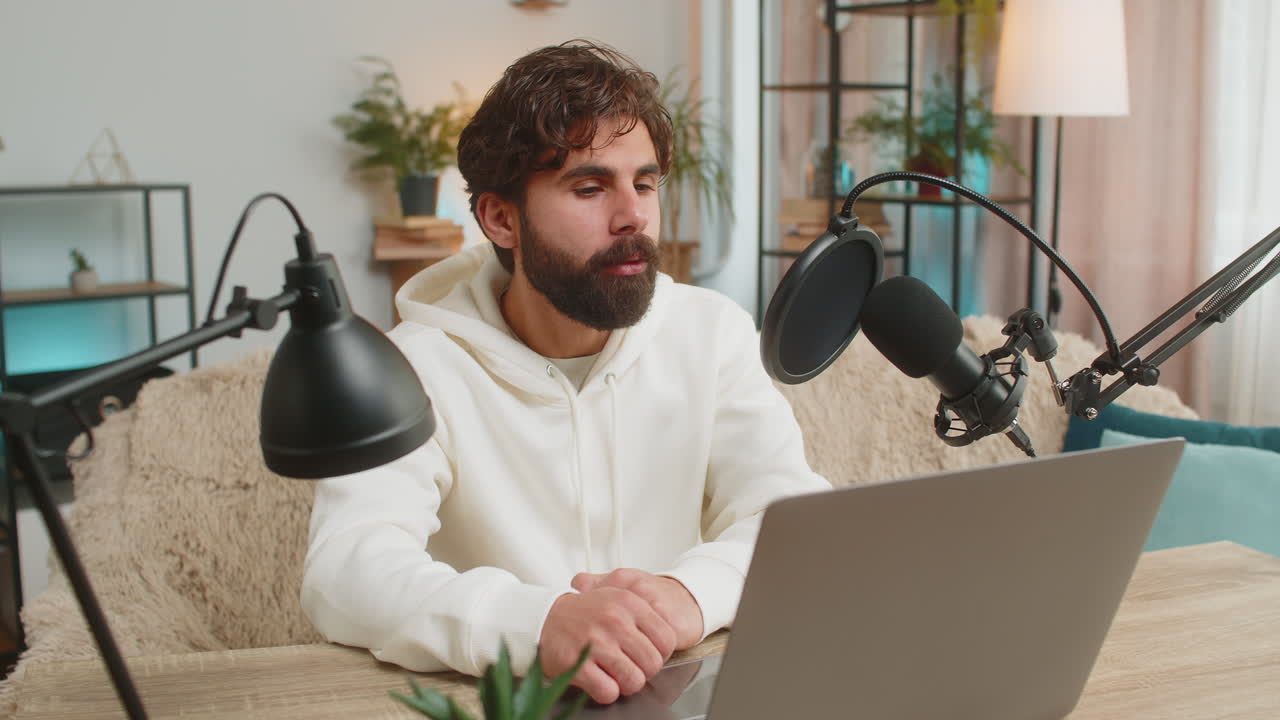 Happy indian blogger man recording podcast on sofa giving workshop webinar sitting on sofa at home