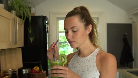 close up of young woman drinking green fruit smoothie