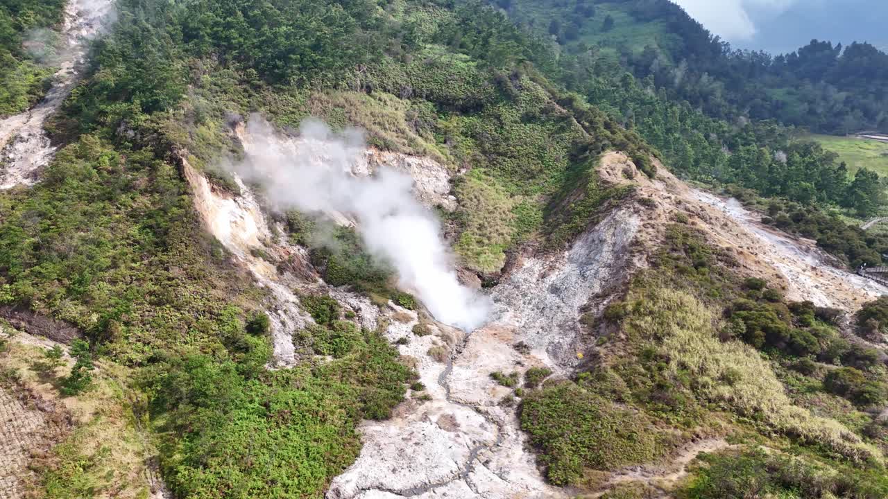 Drone view of a steaming volcanic crater producing sulfur gas surrounded by natural forest hills