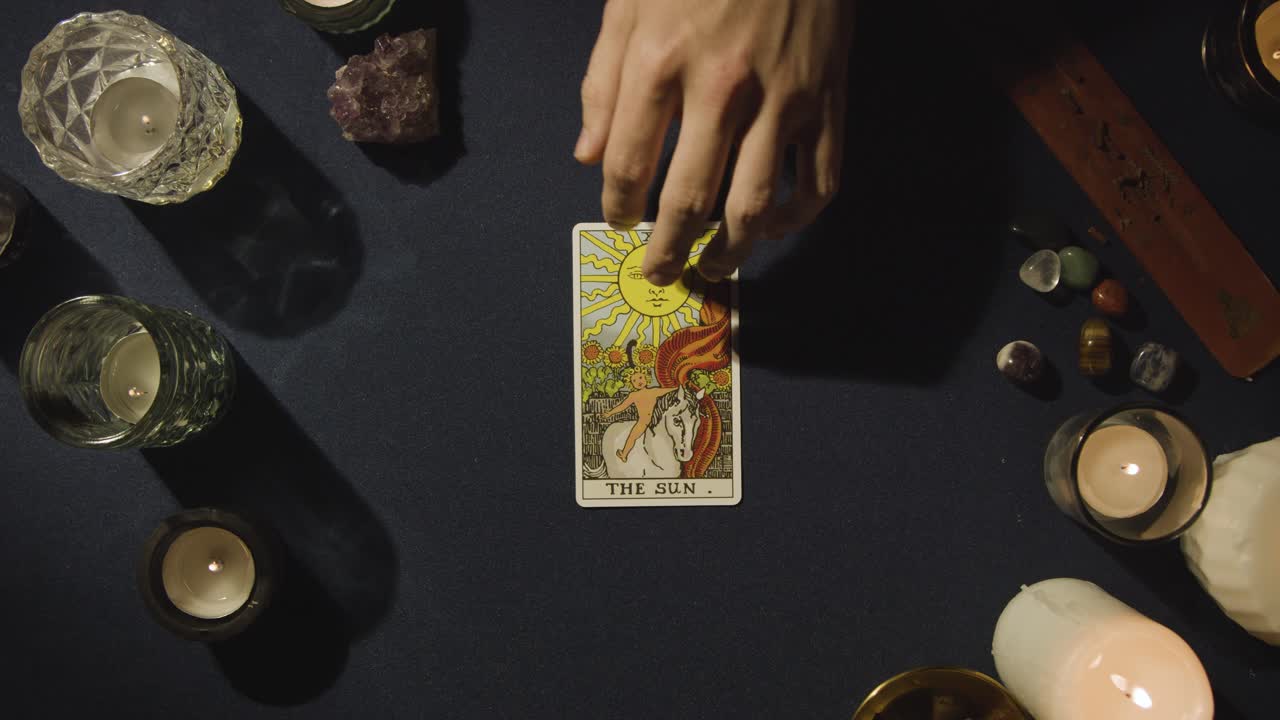 toma aérea de una persona que da lectura de cartas del tarot colocando la carta del sol en la mesa