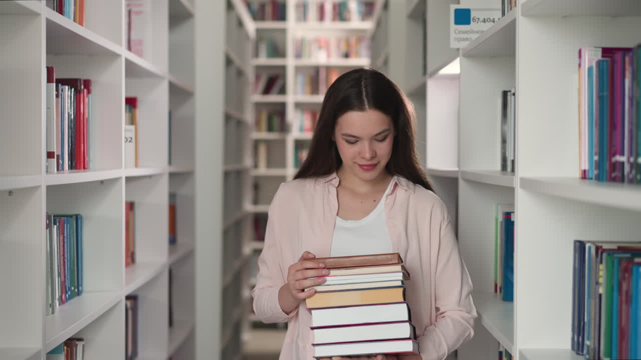 una mujer joven sostiene libros en la biblioteca de la universidad. un estudiante alegre reúne una pila de literatura para escribir su tesis en la librería. una bibliotecaria de cabello largo trabaja en la tienda.