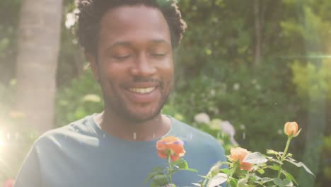Animation-of-glowing-lights-over-african-american-man-smelling-flowers-in-garden