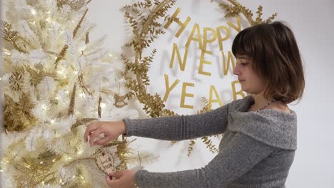 Holiday-tree-decorating-as-a-girl-places-an-ornament-on-a-white-and-gold-Christmas-tree