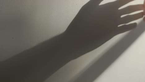 Man's-hand-moves-over-a-wall-with-long-shadow-from-window