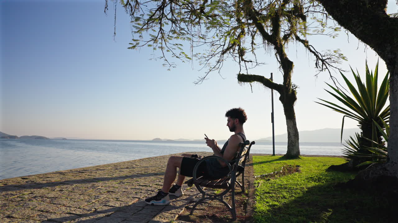 Lonely man sitting on waterfront checking his smartphone