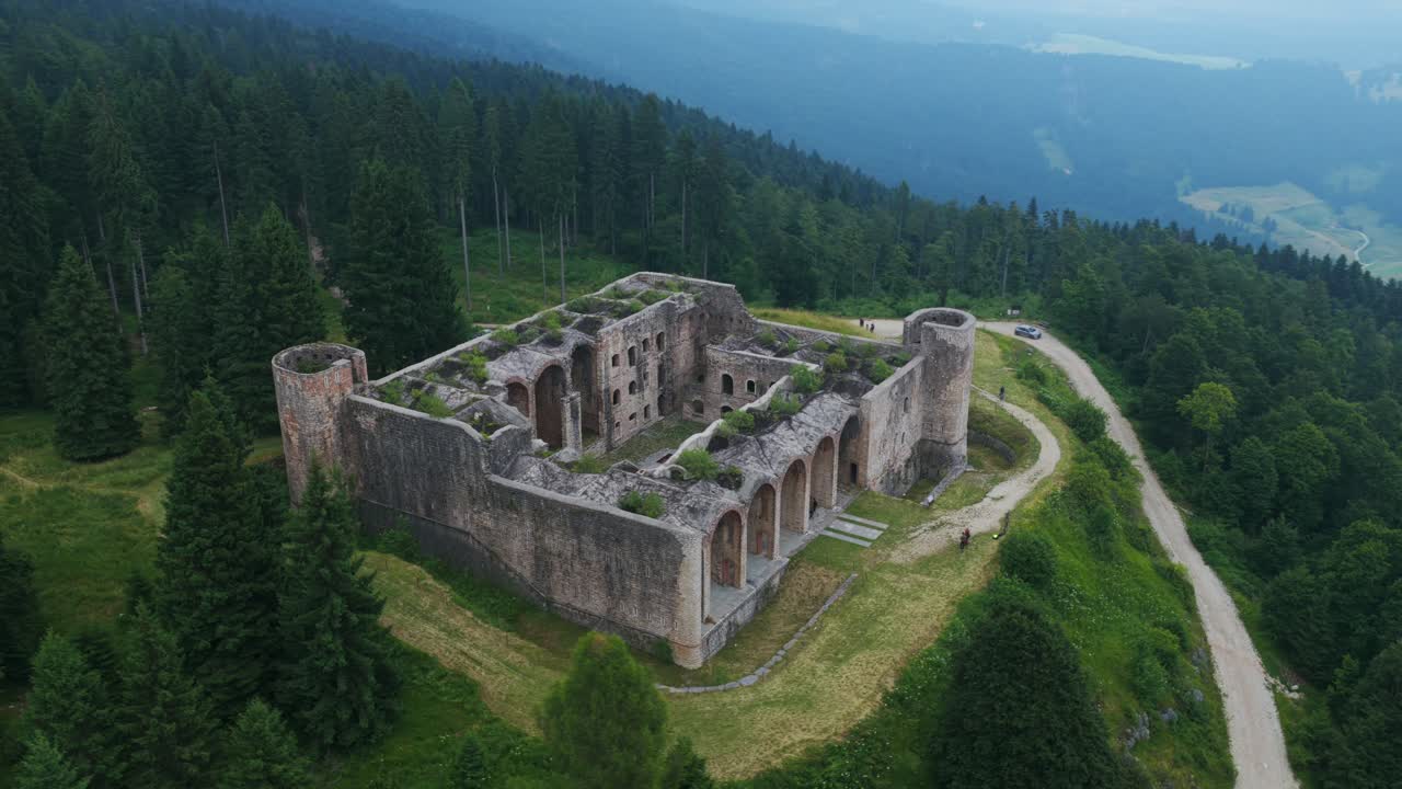 Aerial view of historic Forte Interrotto ruins on hilltop. Overgrown fortress surrounded by pine forest, overlooking valley. For travel or history content, Asiago, Italy