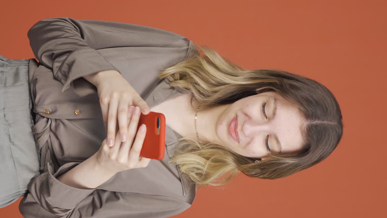 행복한 젊은 여성이 전화로 문자 메시지를 보내는 수직 비디오. 미소.