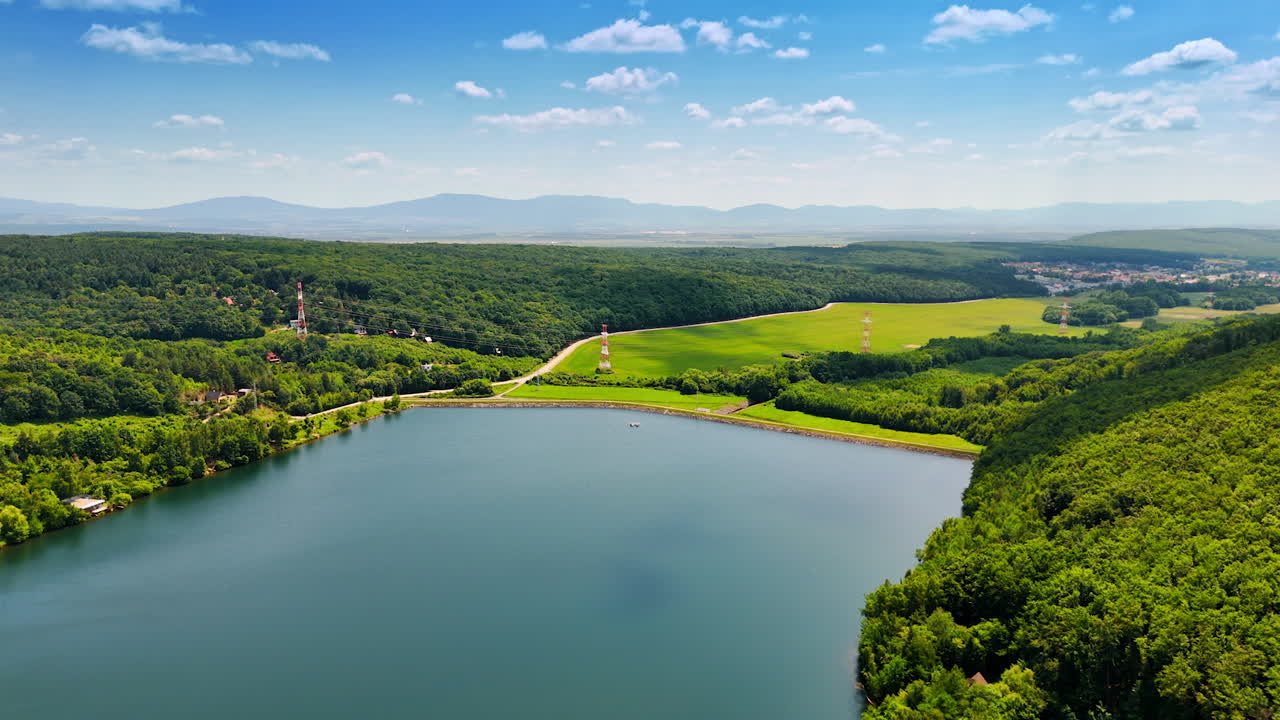 Lush green European landscape. Lush green hills surround a tranquil lake under a bright blue sky. The scene captures the serenity of nature
