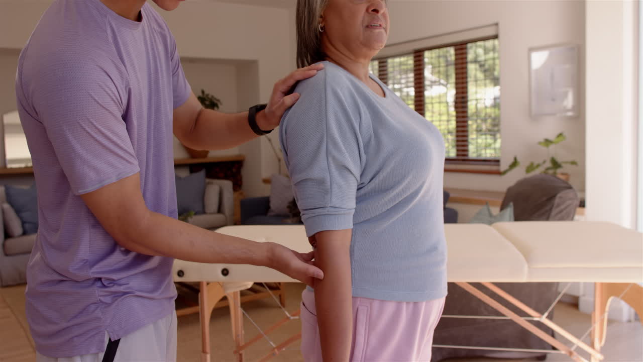 Physiotherapist assisting senior woman with arm exercises in living room