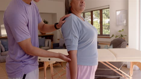 physiotherapist assisting senior woman with arm exercises in living room