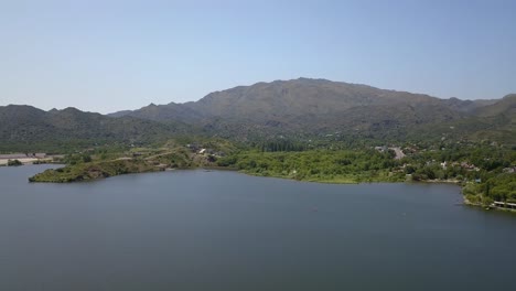 Aerial-view-of-lake-in-summer-with-green-mountains-behind-in-San-Luis,-Argentina