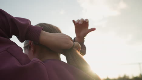 vista trasera de una mujer atando el cabello hacia atrás con la mano, la luz del sol crea un brillo suave alrededor de su mano, la suave luz del sol brilla mientras se prepara para participar en una actividad al aire libre, con un ambiente natural