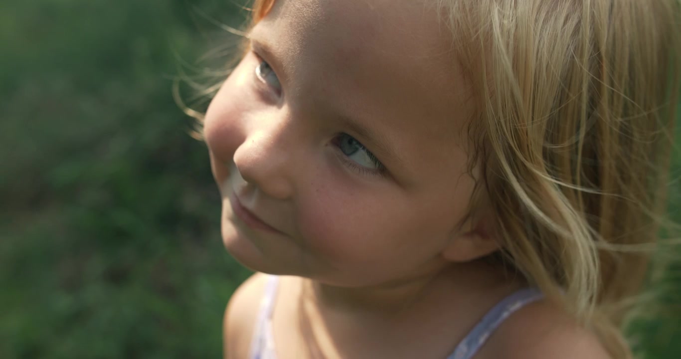 A cheerful close-up of a little girl smiling in a natural outdoor setting. The image radiates warmth and joy.