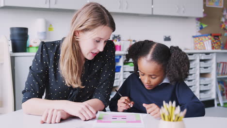 Female-primary-school-teacher-working-one-on-one-with-a-schoolgirl-in-a-classroom,-close-up