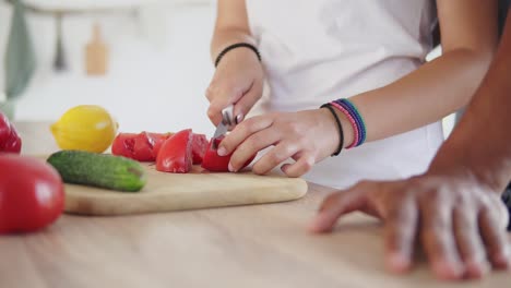 close up view of woman's hands cutting tomato while his boyfriends hands on the table. happy multi ethnic couple in the kitchen