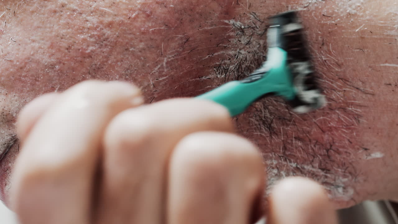 Close up of a man shaving his beard with a razor